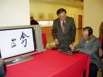 Chang Ben-hang, the director of the Research Office of Calligraphy at Carrie Chang Fine Arts Center is exhibiting his invention “e-calligraphy” at Chung-Cheng Art Gallery. Baseball celebrity Wang Chen-chi (right) visits the exhibition and writes down “chi li.” ( picture offered by Chang Ben-hang )